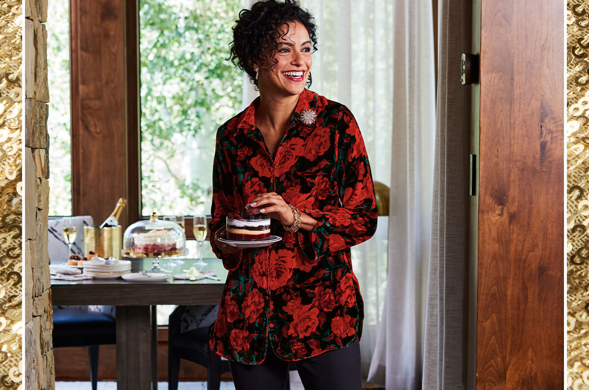 Image of a woman setting the dinner table while wearing the red and black rose printed Icon Silk Velvet Poets Tunic Shirt